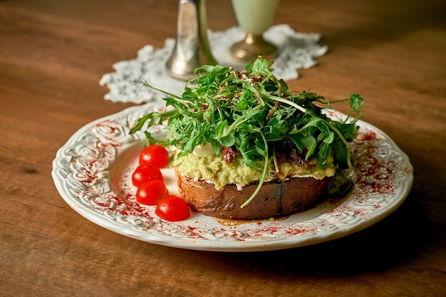 Panino toast appetitoso: pane, avocado, crema di formaggio, mini mozzarella, pomodori secchi, rucola, microgreen.