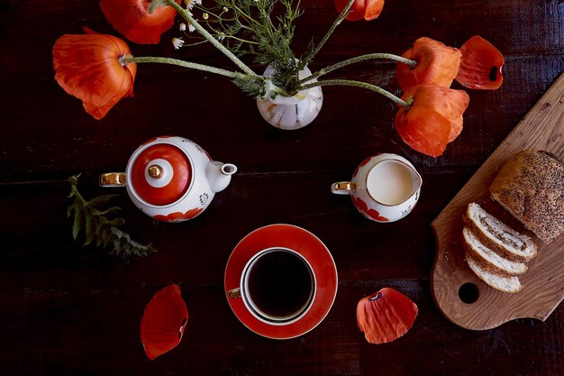 Panino tradizionale con semi di papavero con tazza di tè e latte vicino a fiori di papavero e piatti con papaveri