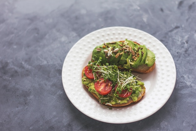 Panino vegano di avocado con microgreens su un piatto bianco su una superficie grigia