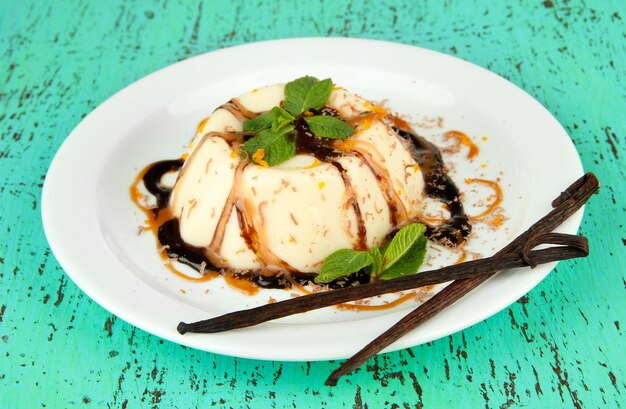 Panna Cotta con salsa di cioccolato e caramello e baccelli di vaniglia su fondo di legno colorato