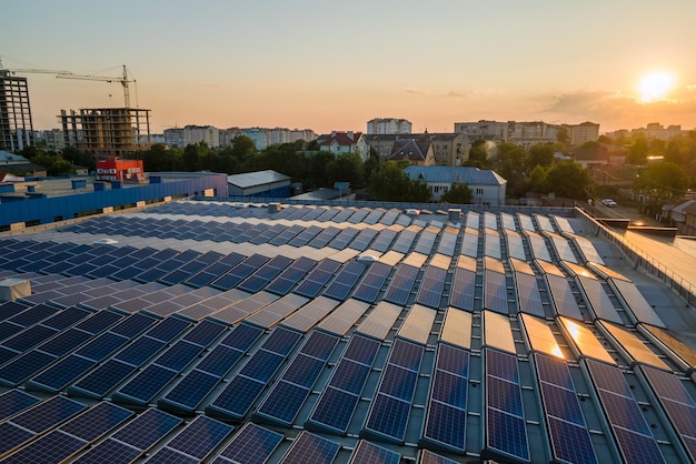 Pannelli solari fotovoltaici blu montati sul tetto dell'edificio per la produzione di elettricità ecologica pulita al tramonto Concetto di produzione di energia rinnovabile