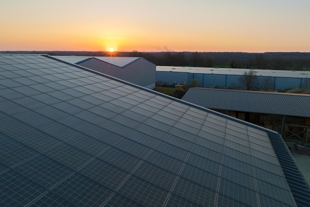 Pannelli solari fotovoltaici blu montati sul tetto dell'edificio per la produzione di elettricità ecologica pulita al tramonto Concetto di produzione di energia rinnovabile