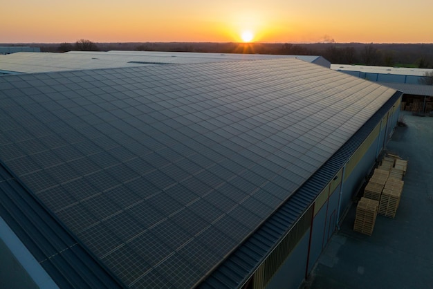 Pannelli solari fotovoltaici blu montati sul tetto dell'edificio per la produzione di elettricità ecologica pulita al tramonto Concetto di produzione di energia rinnovabile