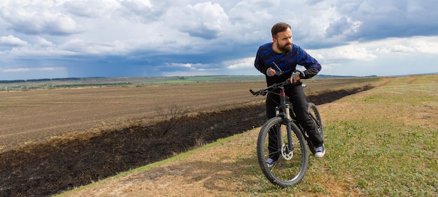 Panorama Ciclista barbuto su una mountain bike in un campo