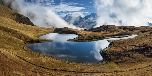 Panorama del lago di montagna Bellissimo paesaggio con cime e nuvole Lago Koruldi Cresta principale del Caucaso Zemo Svaneti Georgia