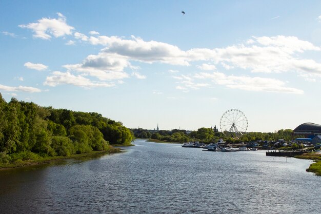 Panorama del paesaggio dall'argine dell'ampio fiume, cielo azzurro, nuvole bianche, ruota panoramica sullo sfondo. Yaroslavl, Russia, centro città