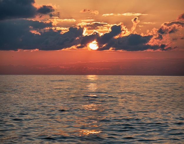 Panorama del sole nelle nuvole scure e nella superficie dell'acqua di mare al tramonto