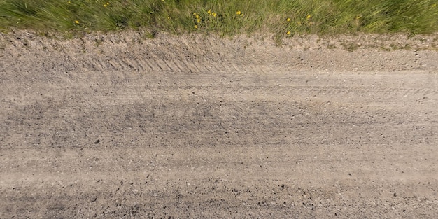 Panorama della superficie dall'alto della strada sterrata con tracce di pneumatici per auto con bordo della strada ed erba