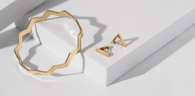 Panorama di bracciale a forma di zig zag e orecchini a triangolo su podio bianco con spazio per la copia