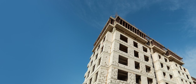 Panorama di un edificio residenziale a più piani in costruzione e gru su uno sfondo di cielo blu