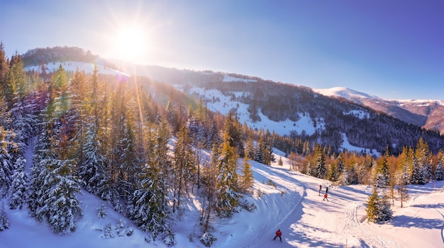 Panorama invernale pittoresco di colline di montagna coperte di neve e abeti in una giornata di sole limpido con il sole e il cielo blu. Concetto di bellezza della natura incontaminata. Copyspace