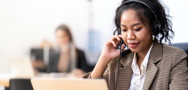 Panorama Operatore di fiducia amichevole dei giovani adulti Razza mista di donna asiatica africana con auricolari che lavorano in un call center