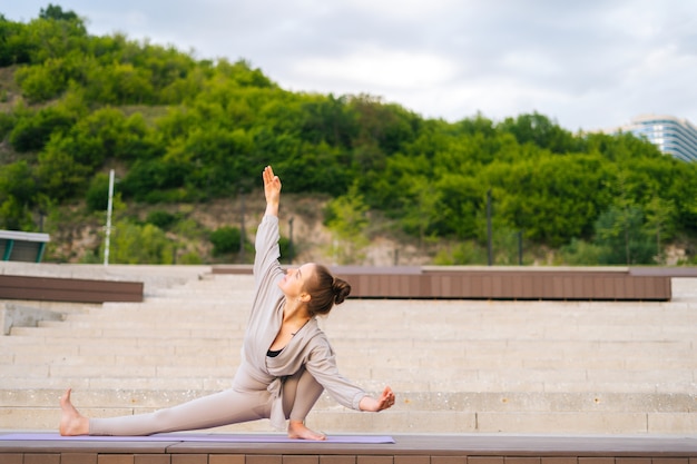 Panoramica di una giovane donna yogini flessibile che pratica esercizi di yoga sul tappetino fitness il giorno d'estate