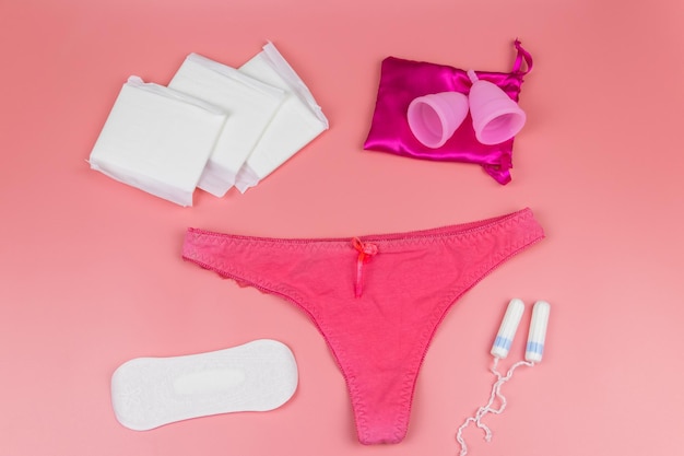 Pantaloncini da donna con tazze mestruali assorbenti igienici e tamponi su sfondo rosa pastello Vista superiore Concetto di giorni critici mestruazione igiene femminile