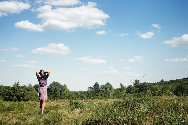 Pantaloni a vita bassa della bella donna che camminano al campo estivo verde sullo sfondo dello spazio del cielo blu per il testo