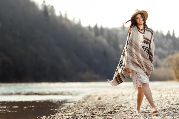 Pantaloni a vita bassa della bella donna che camminano sulla spiaggia del fiume in montagna divertendosi e godendo dello spazio di concetto di viaggio di boho per testo