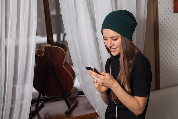 Pantaloni a vita bassa della donna in cappello verde che ascolta musica e si gode la vita