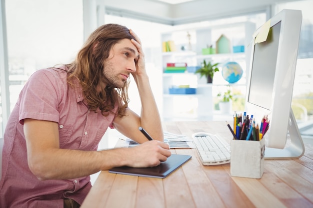 Pantaloni a vita bassa stanco che lavorano alla tavola e al computer di grafici