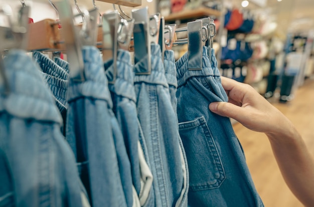 Pantaloni del denim dello shopping della donna nel negozio di abbigliamento Donna che sceglie i vestiti Jeans sull'impiccagione del gancio