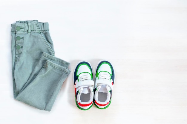 Pantaloni jeans con scarpe da ginnastica Set di vestiti e accessori per bambini per la primavera, l'autunno o l'estate su sfondo bianco Abito per bambini alla moda Vista dall'alto piatta vista dall'alto