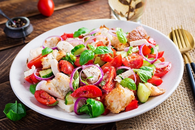 Panzanella toscana, tradizionale insalata italiana con pomodori e pane su fondo di legno. Insalata di panzanella vegetariana. Cibo sano mediterraneo.