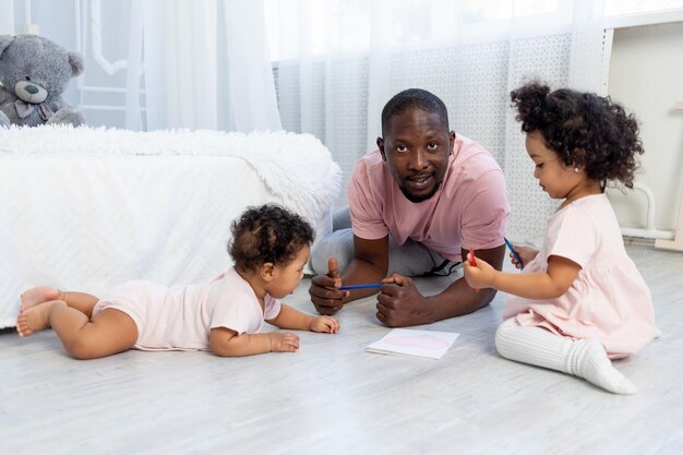 Papà afroamericano insegna ai bambini come disegnare le matite sul pavimento di casa