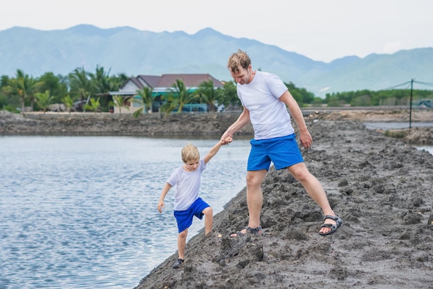 Papà aiuta il figlio a scendere al lago L'acqua spiega le regole di sicurezza Famiglia insieme a piedi Gioca a casa educazione naturale del bambino festa del papà responsabilità paterne influenza sulla formazione del figlio visione del mondo