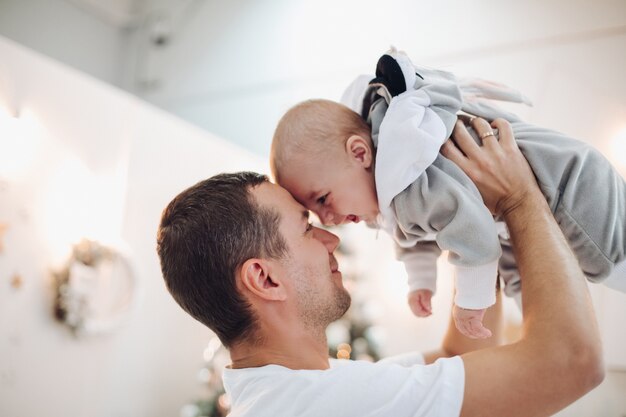 Papà amorevole che tiene il figlio sveglio del bambino tra le braccia faccia a faccia a mezz'aria. Bambino sorridente in costume da coniglietto.