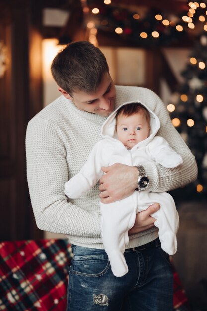 Papà amorevole in maglione bianco che gioca con un neonato che lo tiene in aria tra le braccia