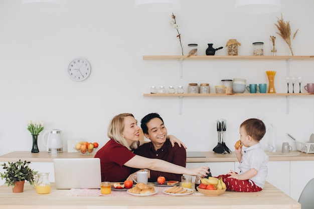 Papà asiatico e mamma europea lavorano con i loro gadget e il figlio fa colazione da solo. Moderni problemi tecnologici.