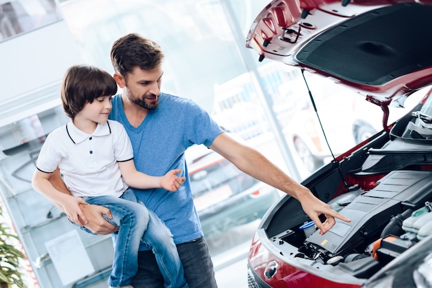 Papà con suo figlio in braccio mostra come funziona il motore in macchina.