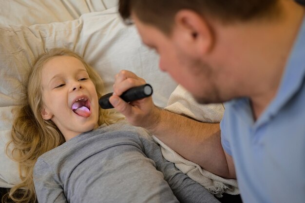 papà controlla la gola del suo bambino malato accende una torcia in modo che sia meglio vedere