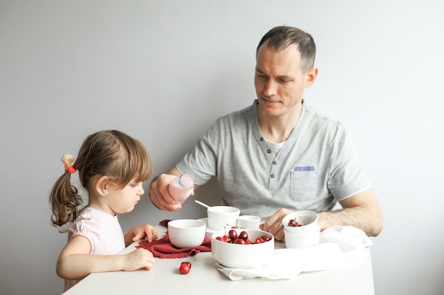 Papà dà da mangiare a una piccola figlia carina una sana colazione a casa su uno sfondo chiaro. Famiglia felice