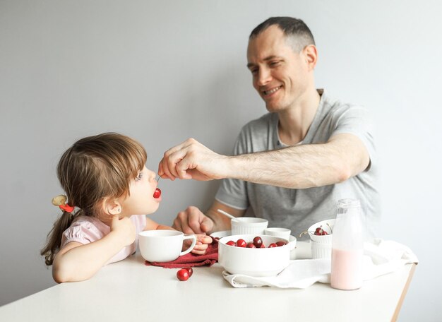 Papà dà da mangiare a una piccola figlia carina una sana colazione a casa su uno sfondo chiaro. Famiglia felice