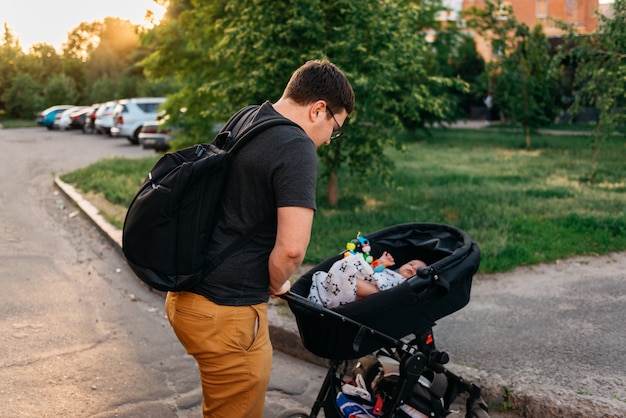 Papà del padre con il passeggiatore neonato della carrozzina fuori durante il tramonto di sera di estate