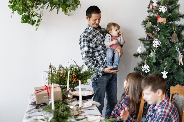 Papà di famiglia con suo figlio vicino all'albero di Natale a casa Colazione in famiglia a Natale Il padre mostra a suo figlio una casa di Natale di abete