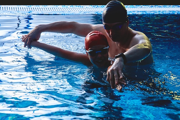 Papà e allenatore insegnano al figlio del ragazzo a nuotare, divertirsi, giocare e tuffarsi in una piscina blu