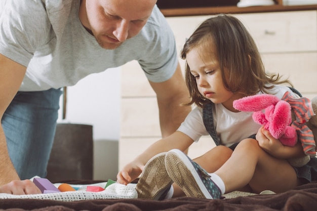 Papà e bambina 2-4 giocano con il costruttore e i peluche, seduti per terra a casa