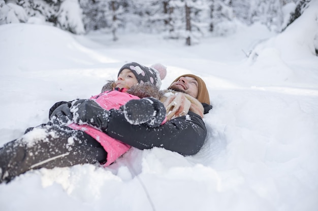 Papà e bambina sdraiati sulla neve nel parco invernale