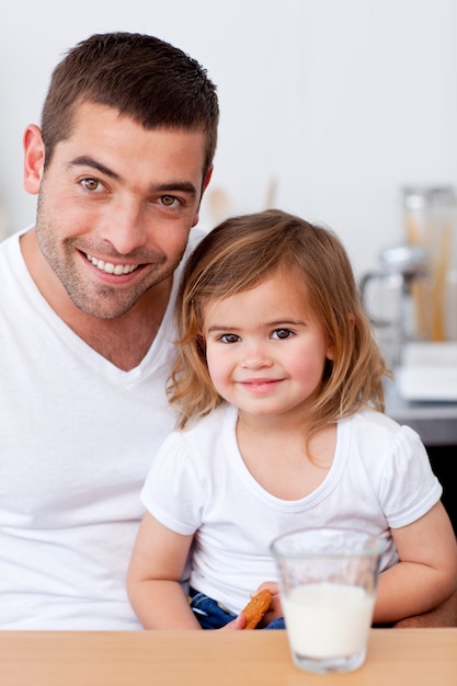 Papà e bambina sorridenti che mangiano i biscotti con latte