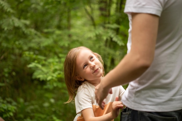 Papà e figlia camminano nella foresta in estate, la ragazza tiene la mano del papà e lo guarda negli occhi