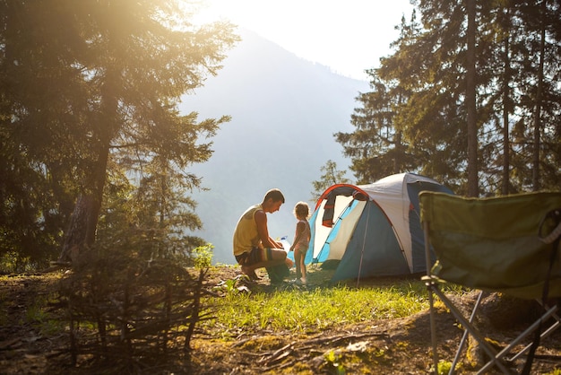 Papà e figlia di 2 anni vicino a una tenda in un campeggio nella foresta in montagnaFamiglia attività ricreative all'aperto avventure ecocompatibili sopravvivenza in natura