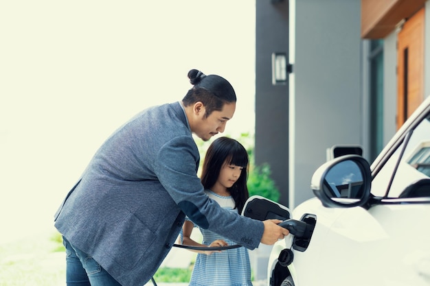 Papà e figlia progressisti che caricano l'auto EV dalla stazione di ricarica domestica