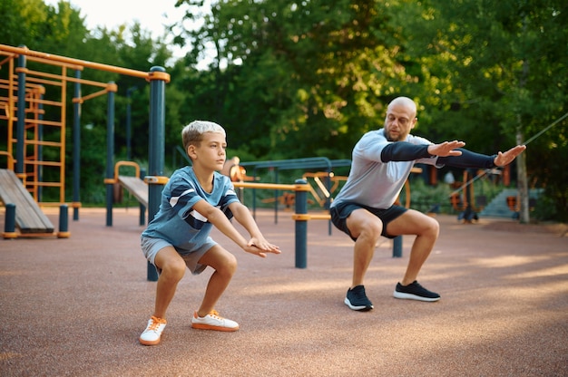 Papà e figlio che fanno esercizio, allenamento sportivo nel parco giochi all'aperto. La famiglia conduce uno stile di vita sano, allenamento fitness nel parco estivo