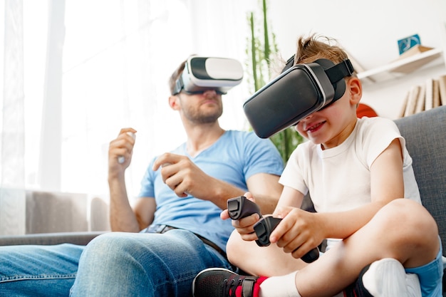 Papà e figlio che si siedono sul divano e giocano insieme con gli occhiali VR