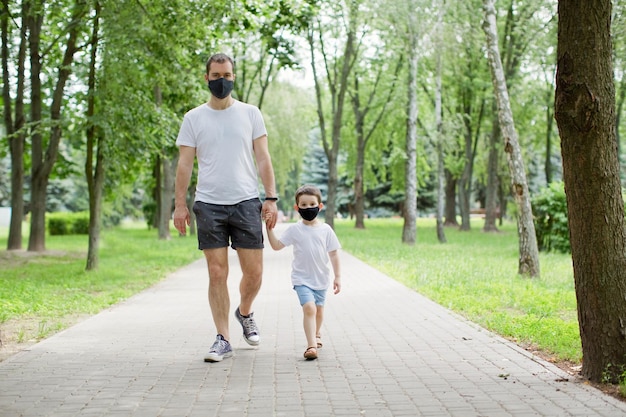 Papà e figlio con maschere nere che camminano nel parco Concetto di allontanamento sociale e quarantena