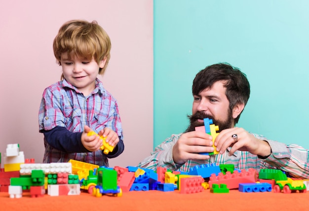 Papà e figlio costruiscono blocchi di plastica. Giocattolo utile. Sviluppo e educazione della cura dei bambini. Padre figlio gioco. Padre e figlio creano costruzioni colorate con i mattoni. Il padre e il ragazzo barbuti giocano insieme.