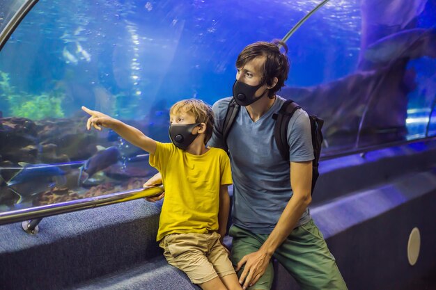 Papà e figlio in maschere mediche guardano il pesce nell'acquario nell'oceanario la gente cammina in medicina