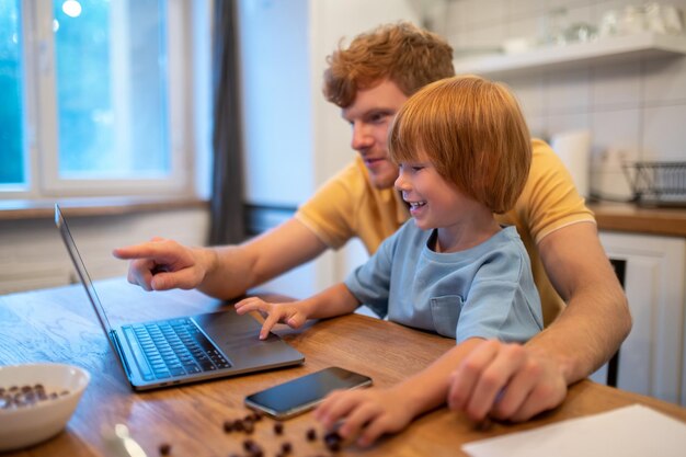 Papà e figlio seduti al tavolo e guardando qualcosa insieme