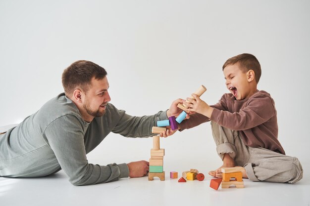 Papà e figlio sorridenti divertendosi e giocando giocattoli di mattoni colorati su sfondo bianco Padre premuroso di paternità con il suo bambino